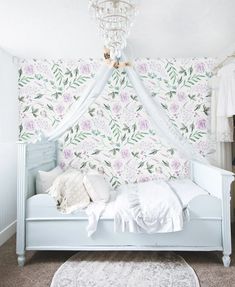 a white bed sitting under a chandelier next to a wall covered in flowers