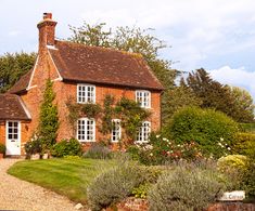 a brick house surrounded by greenery and flowers on a sunny day in the country