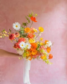 a woman holding a bouquet of flowers in her hand on a pink background with white and orange colors