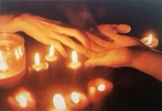 several people are holding hands over candles