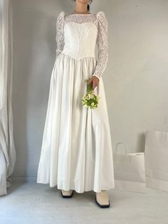 a woman wearing a white dress and holding a bouquet in front of a window with curtains behind her