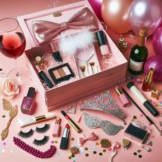 a pink box filled with makeup and other items next to balloons, confetti, wine glasses and candles