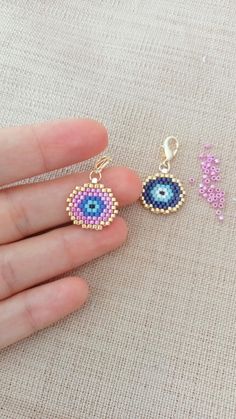 the hand is holding two earrings with evil eyes on them, and one has an evil eye