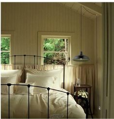 a bed with white sheets and pillows in a room next to two windows, one is hanging from the ceiling