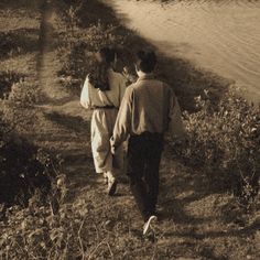 two people walking down a path near the water