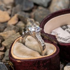 an engagement ring sits in a velvet box on some rocks and stones, with the wedding band wrapped around it