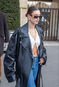 a woman in black leather jacket and jeans walking down the street with her hand on her hip