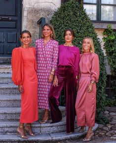 three women standing next to each other in front of a building with steps and bushes