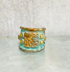 a green and gold vase sitting on top of a white table next to a wall