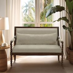 a couch sitting in front of a window next to a potted plant