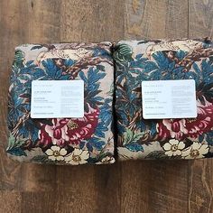 two pillows with floral designs on them sitting on a wooden floor next to each other