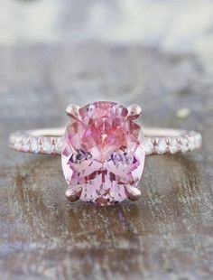 a pink diamond ring with diamonds around it on a wooden surface in front of a brick wall