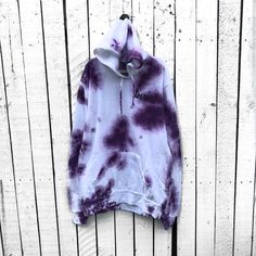 a purple and white tie dye hoodie hanging on a wooden wall