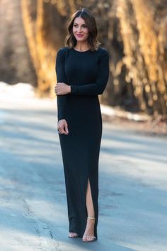 a woman standing in the middle of a road wearing a long black dress and heels