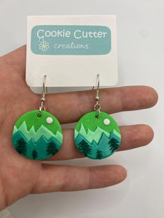 a pair of green and white earrings with trees on them in front of a card