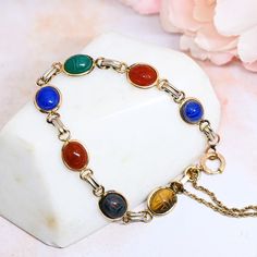 Lovely vintage 12k gold filled* scarab bracelet featuring 7 smaller genuine semiprecious stones, including tiger's eye, (a less-common) bloodstone, carnelian, green and blue chalcedony, and onyx. Main clasp is a beautiful decorative thumbless sport clasp. The smaller safety clasp (it is not clasped in the correct spot in the pics, btw) spring is no longer working - it must be closed manually. I will replace with a working vintage GF clasp if the buyer chooses. (Some prefer all the original parts.) 7.5 inches long Good vintage condition. There is some wear/fading to the finish of the connecting links. I am not certain all of these findings are original to the piece (the clasps and chain). Marks: 1/20 12KT GF CT Featured bracelet only. See other scarab pieces in separate listings: https://my Vintage Gold Cabochon Gemstones, Vintage Gold Bracelets With Natural Stones, Scarab Bracelet, Egyptian Revival, Blue Chalcedony, Tiger's Eye, Gold Filled Jewelry, Chain Link Bracelet, Link Bracelets