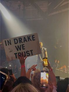 people holding up cell phones in front of a stage with lights and signs on it