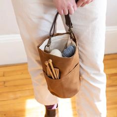 a person holding a brown bag with knitting needles and balls in it