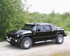 a black suv parked on top of a dirt road next to trees and bushes in the background