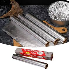 four rolls of aluminum foil sitting on top of a cutting board next to a box of aluminum foil