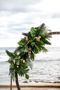 a wedding arch decorated with tropical flowers and greenery on the beach near the ocean