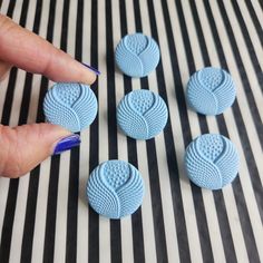 a hand is pointing at four blue buttons on a striped tablecloth with black and white stripes