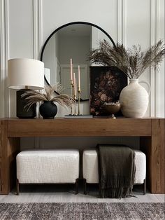 a wooden table topped with a mirror and two vases filled with plants next to a bench