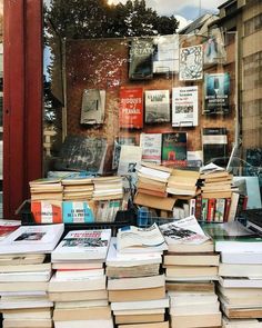 many books are stacked on top of each other in front of a storefront window