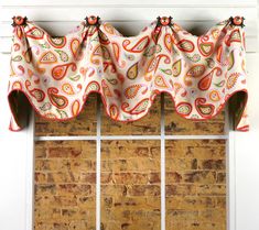 the window valance is decorated with an orange paisley pattern and black trim, along with a white brick wall