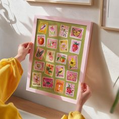 a person holding up a pink and green framed art piece with lots of stamps on it