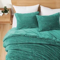 a bed with green comforter and pillows on it in a room next to a night stand