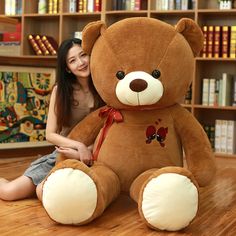 a woman sitting on the floor with a large teddy bear in front of bookshelves