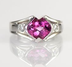 A dazzling pink Tourmaline checkerboard cut from Brazil is is accented with two flush set diamonds in this gorgeous 14k white gold ring. The natural Tourmaline is a 9 x 7 mm oval shape checkerboard cut and weighs 1.93 carats. The two diamonds are round brilliant cuts measuring 2.8mm with a total weight of .16 carats G-H color VS1-2 clarity The ring is 10.5 mm wide (3/8 inch) at the stone tapering down to 3.5 mm The height of the ring is 6 mm Ring weighs 7.31 grams Size 6 3/4 All items from Stowe Pink Platinum Diamond Ring For Anniversary, Formal 14k White Gold Pink Rings, Formal Pink 14k White Gold Rings, Pink 14k White Gold Jewelry With Center Stone, Pink 14k White Gold Wedding Rings, Pink Platinum Wedding Rings, Formal Pink Sapphire Rings With Diamond Cut, Formal Pink Sapphire Diamond Cut Rings, Modern Pink Ring For Formal Occasions