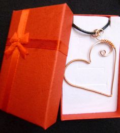 an open red box with a heart shaped pendant in it