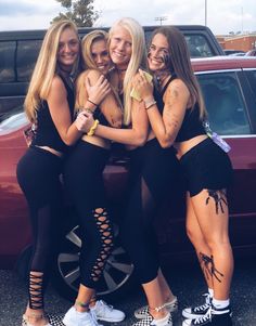 four girls are posing in front of a car with their arms wrapped around each other