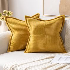 two yellow pillows sitting on top of a white couch next to a vase with flowers