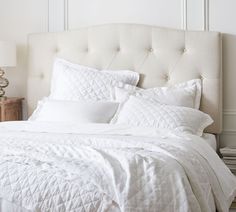 a bed with white sheets and pillows in a bedroom