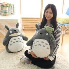 a woman sitting on the floor holding two totoro stuffed animals, both with eyes closed