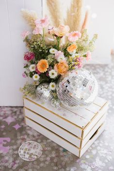 a mirrored disco ball and flowers on a wooden crate in front of a white wall