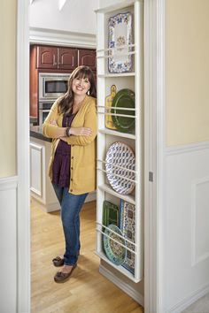 a woman standing in front of a refrigerator with plates on the door and shelves behind her