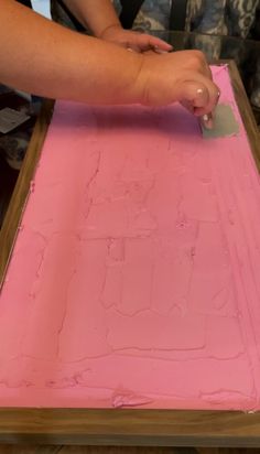 a person is using a knife to cut out the pink paint on a piece of paper