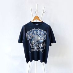 a cowboys t - shirt hanging up on a clothes hanger in front of a white wall