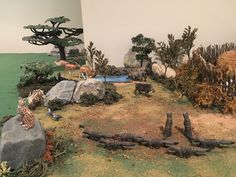 an assortment of animals and plants on display in a room with fake rocks, grass and trees