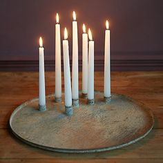 seven white candles are arranged in a circle on a wooden table with a metal tray