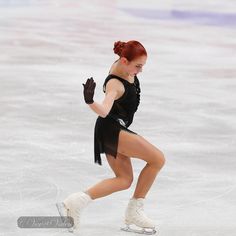 a woman skating on an ice rink wearing a black dress and white boots with her hands in the air