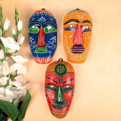 three colorful masks sitting on top of a table next to white flowers and greenery