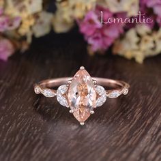 a pink diamond ring sitting on top of a wooden table next to purple and white flowers