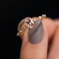 a woman's hand holding a ring with an oval shaped pink diamond on it