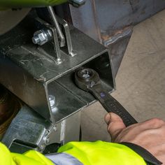 a man in yellow safety vest holding wrench next to metal box with nut and bolt on it