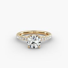 a yellow gold engagement ring with diamonds on the band and a round brilliant cut center stone